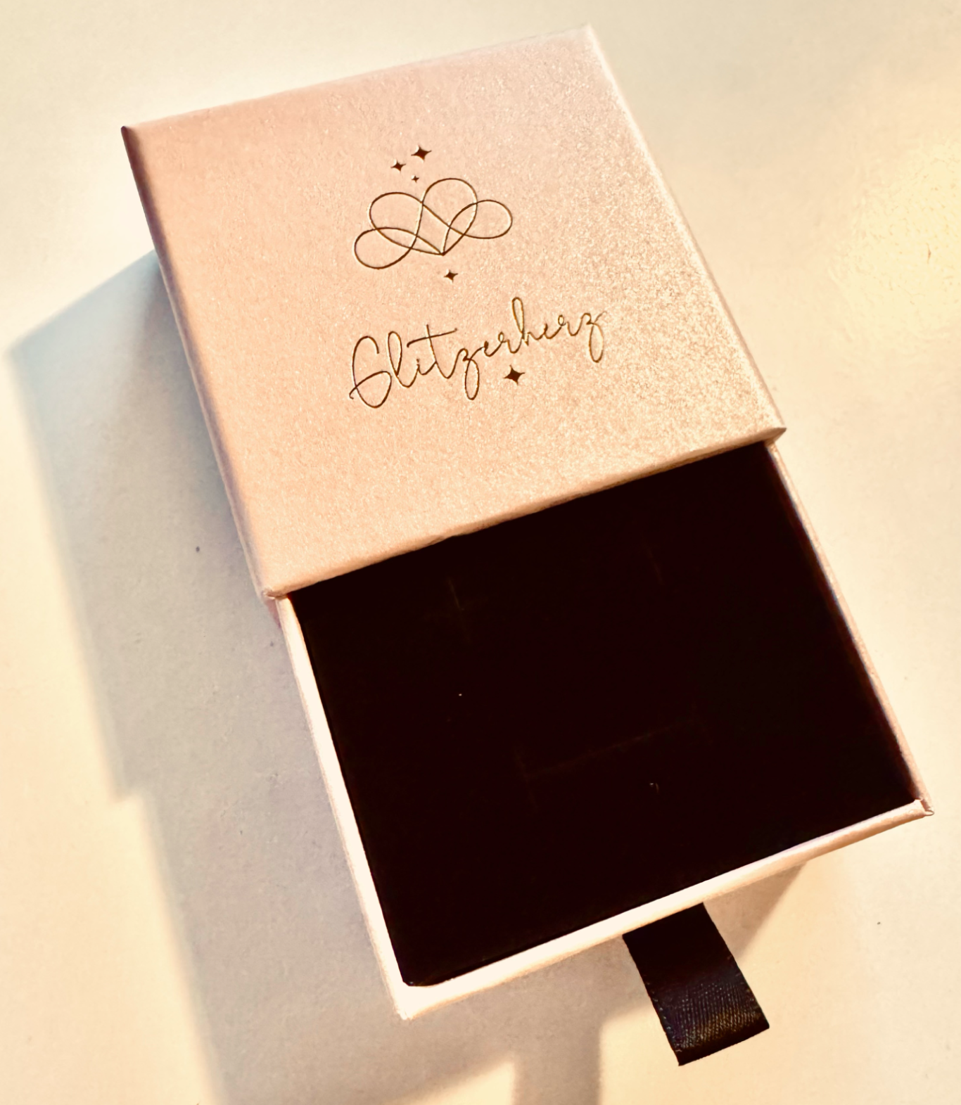 Unsere Glitzerherz Geschenkbox Eine geöffnete Schmuckschatulle mit schwarzer Innenfläche und einem Schriftzug.
